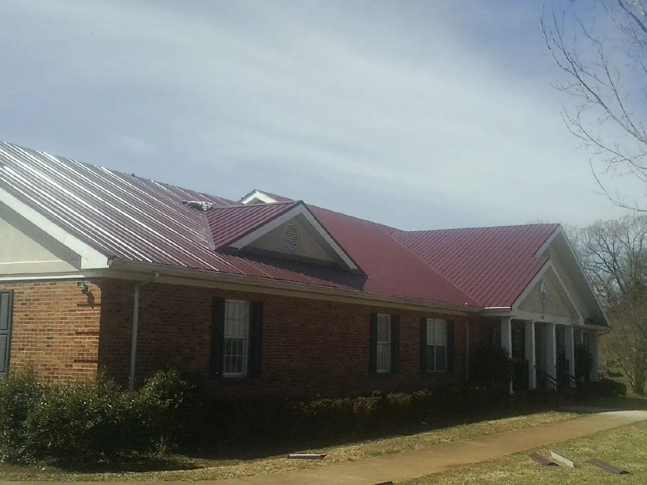 Red metal roof with gabled entries on a long brick building, from a Hail Damage Roof Repair job in Morris