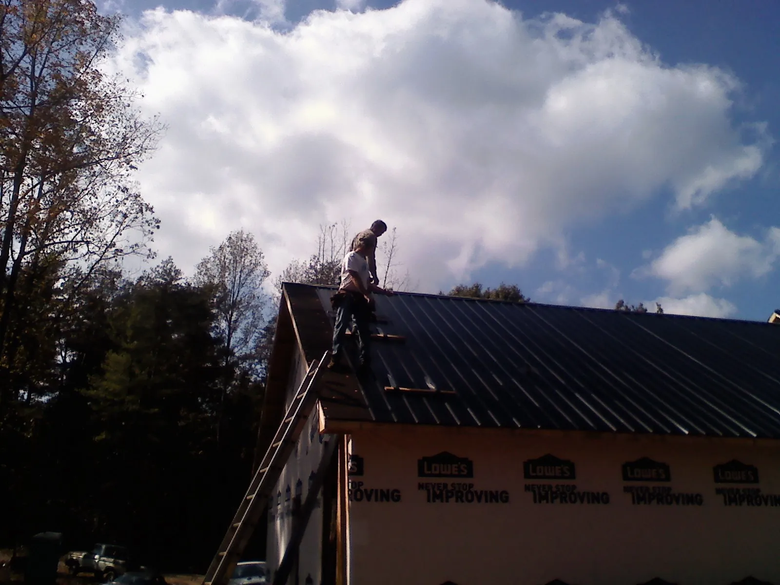 Roofer fastening dark metal panels high against a cloudy sky, from a Roof Inspection job in Morris